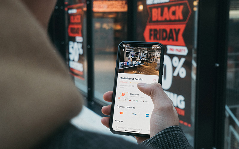 Hand holds phone in front of Black Friday Sale shopfront