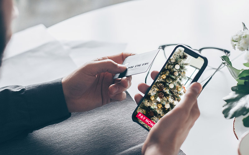 Man holds credit card close to phone online shopping for Christmas tree